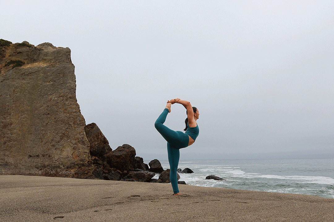 A woman doing a yoga pose on a beach.