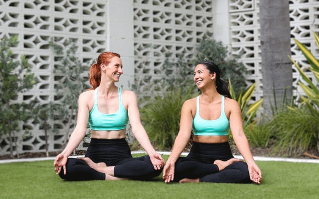 Two women sitting on the grass and doing yoga.