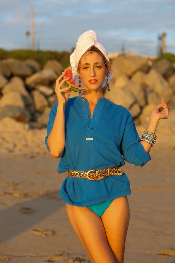 A woman in a blue bikini holding a watermelon on the beach.