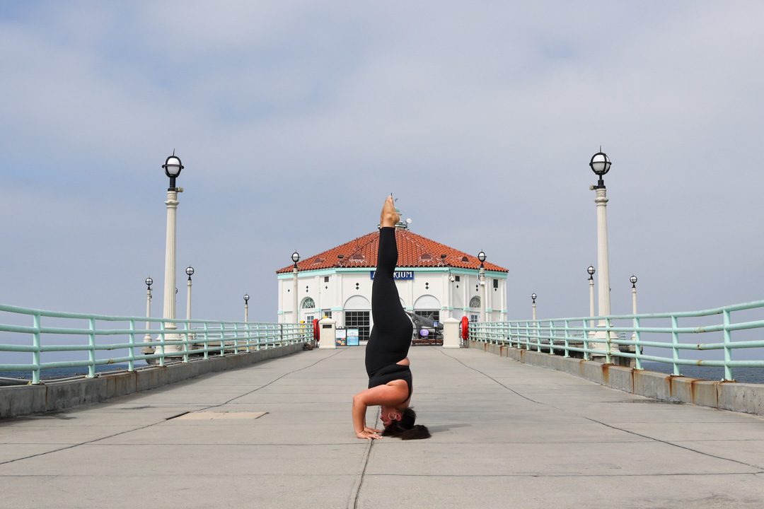 A woman doing a handstand in front of a pier.