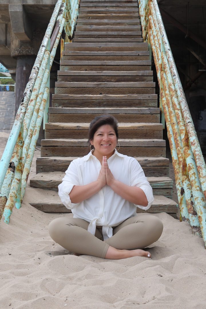 A woman sits on the sand next to a set of stairs.