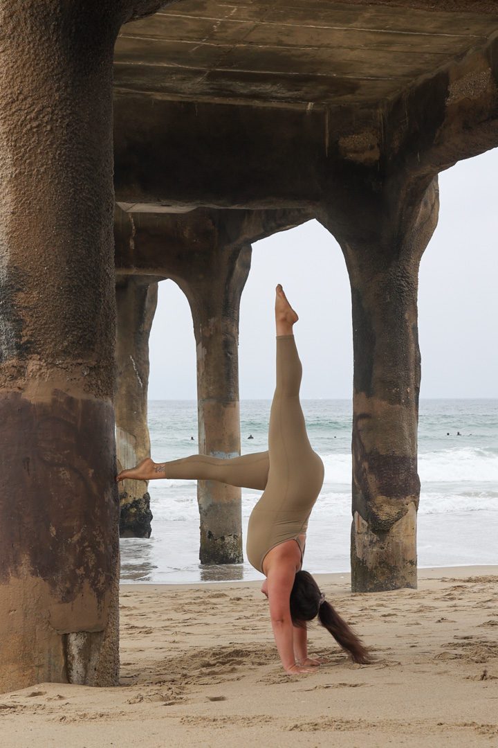 A woman doing a handstand under a pier.