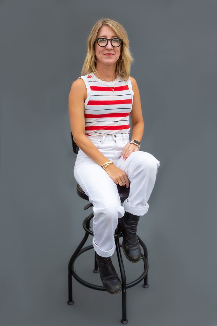 A woman sitting on a stool in a red and white striped top.