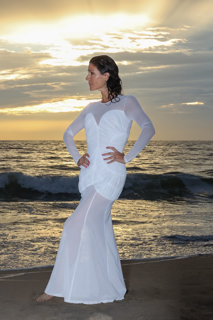A woman in a white dress standing on the beach.