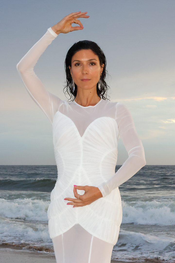 A woman in a white dress posing on the beach.
