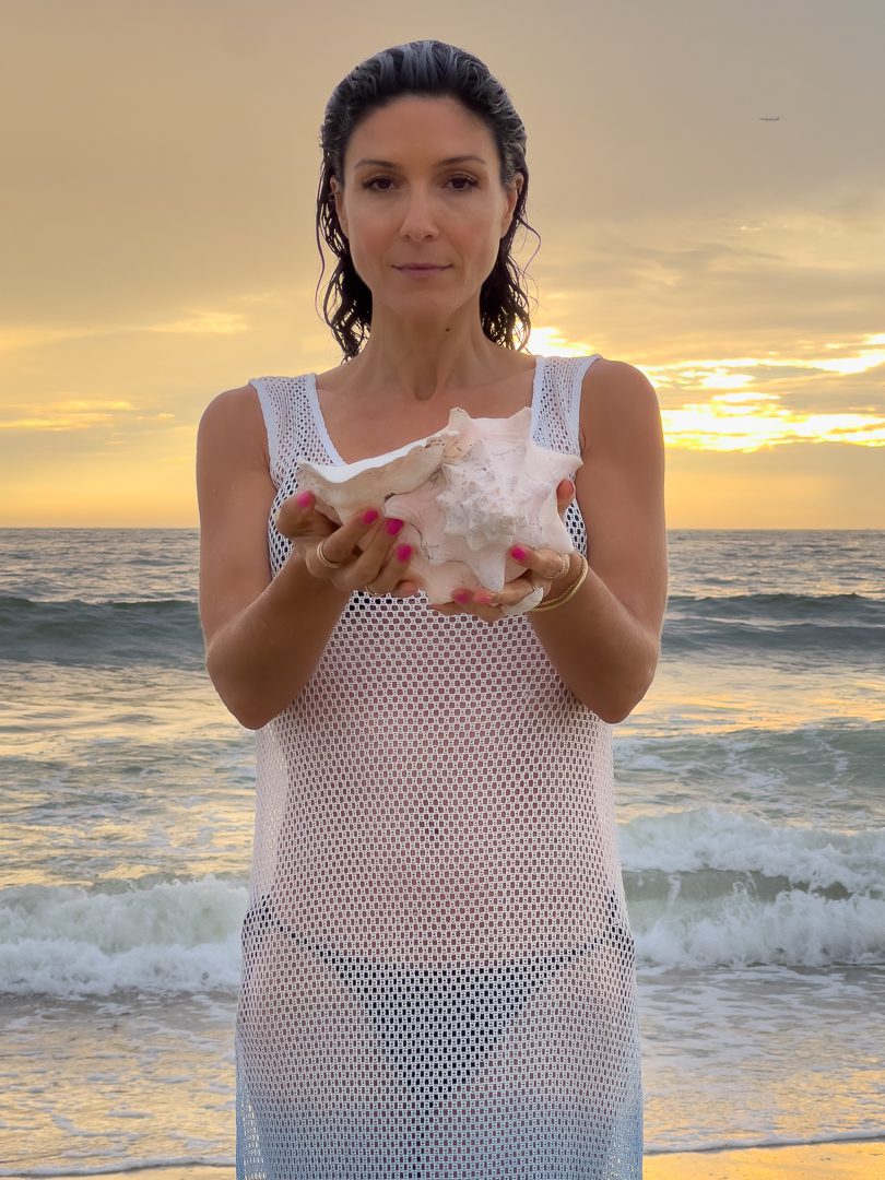 A woman holding a shell on the beach.