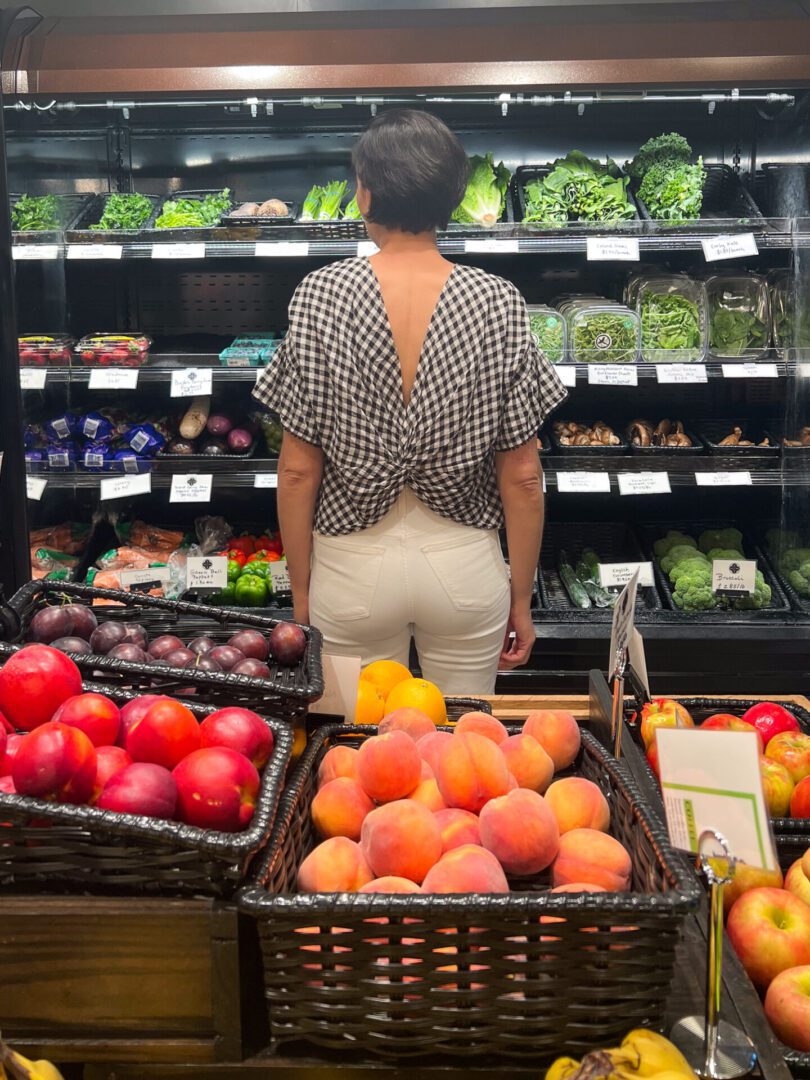 A woman looking at fruits and vegetables in a grocery store.